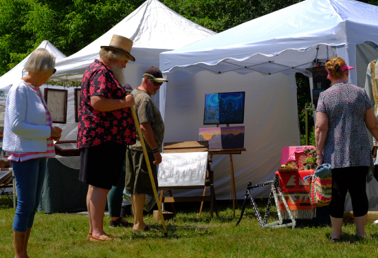 two men and two women standing in front of a white tent looking at some art