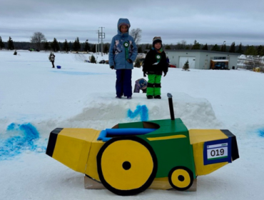 award winners standing next to winning cardboard toboggan shaped like the banana