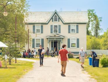 people standing outside historic home at village museum